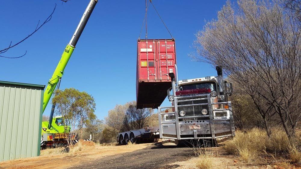 A Red Shipping Container Is Being Lifted Into a Truck by A Crane — Spinifex Container Solutions In Ciccone, NT