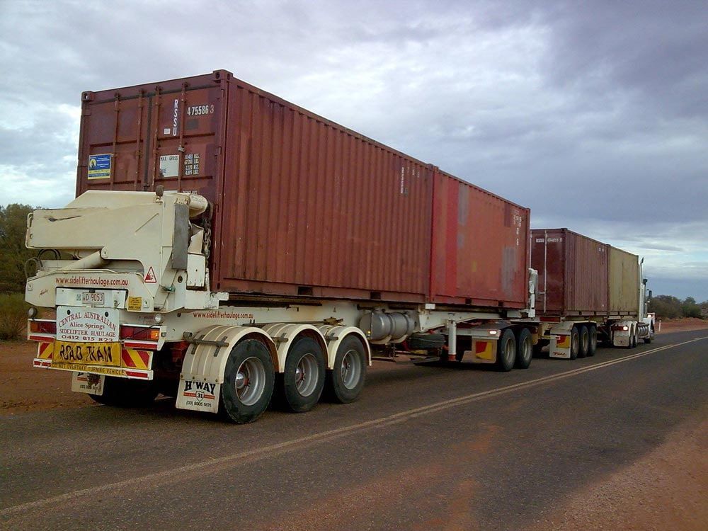 A Semi Truck with A Red Container on The Back Is Driving Down the Road — Spinifex Container Solutions In Ciccone, NT
