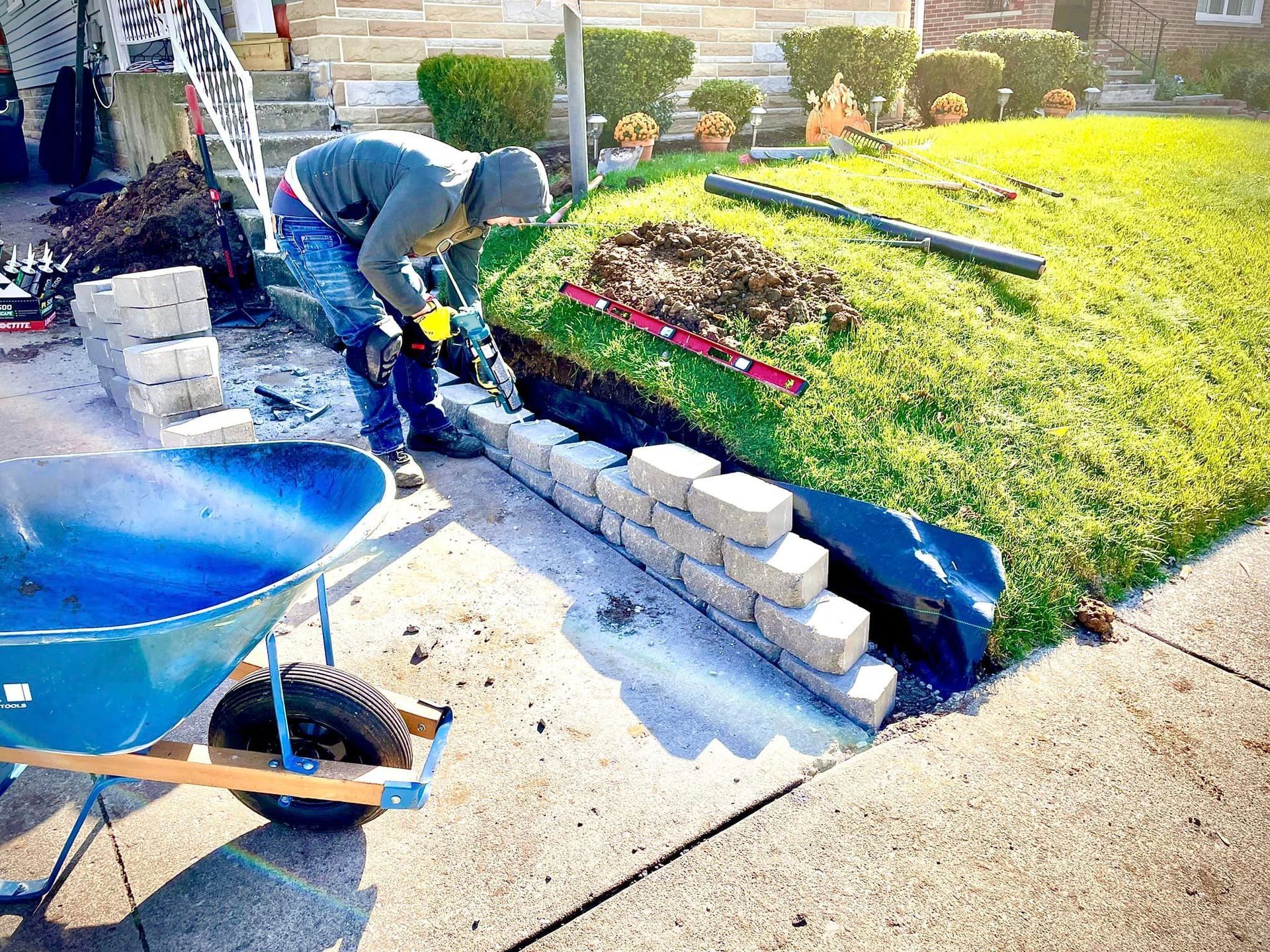 A man is laying bricks on a sidewalk next to a wheelbarrow.