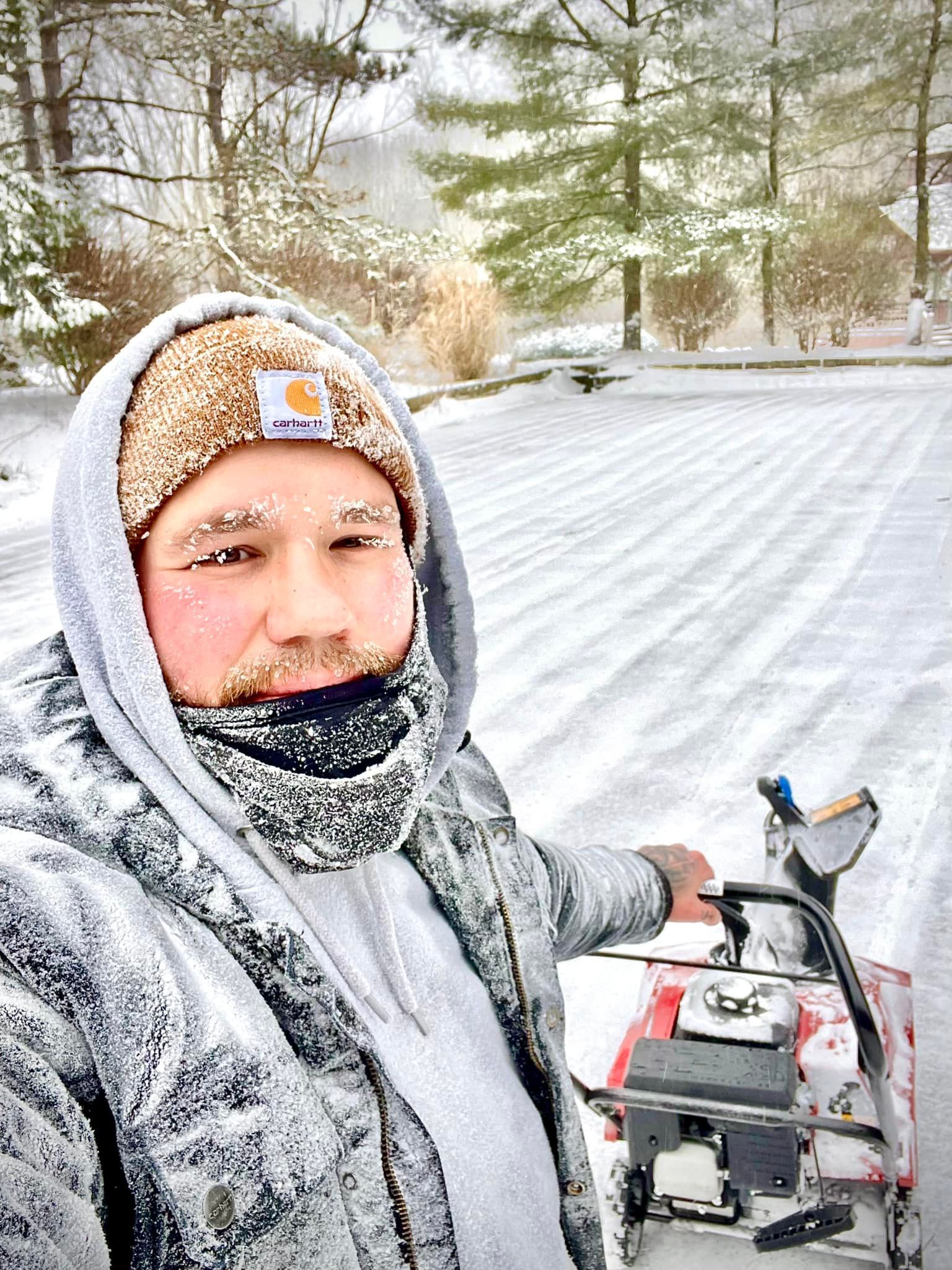 A man is standing in the snow holding a snow blower.