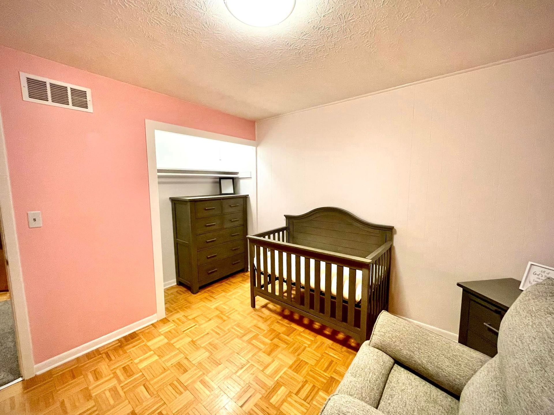 A bedroom with a crib , chair , nightstand and dresser.