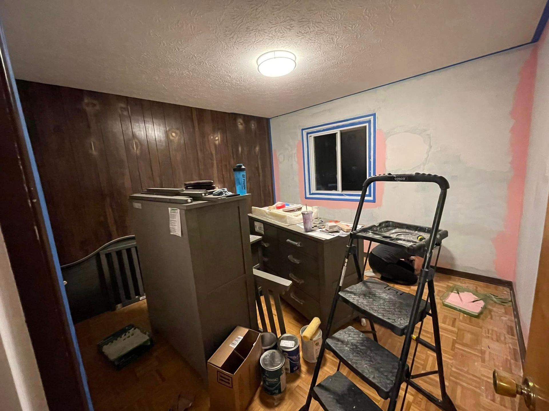 A room with a ladder and boxes on the floor is being painted.