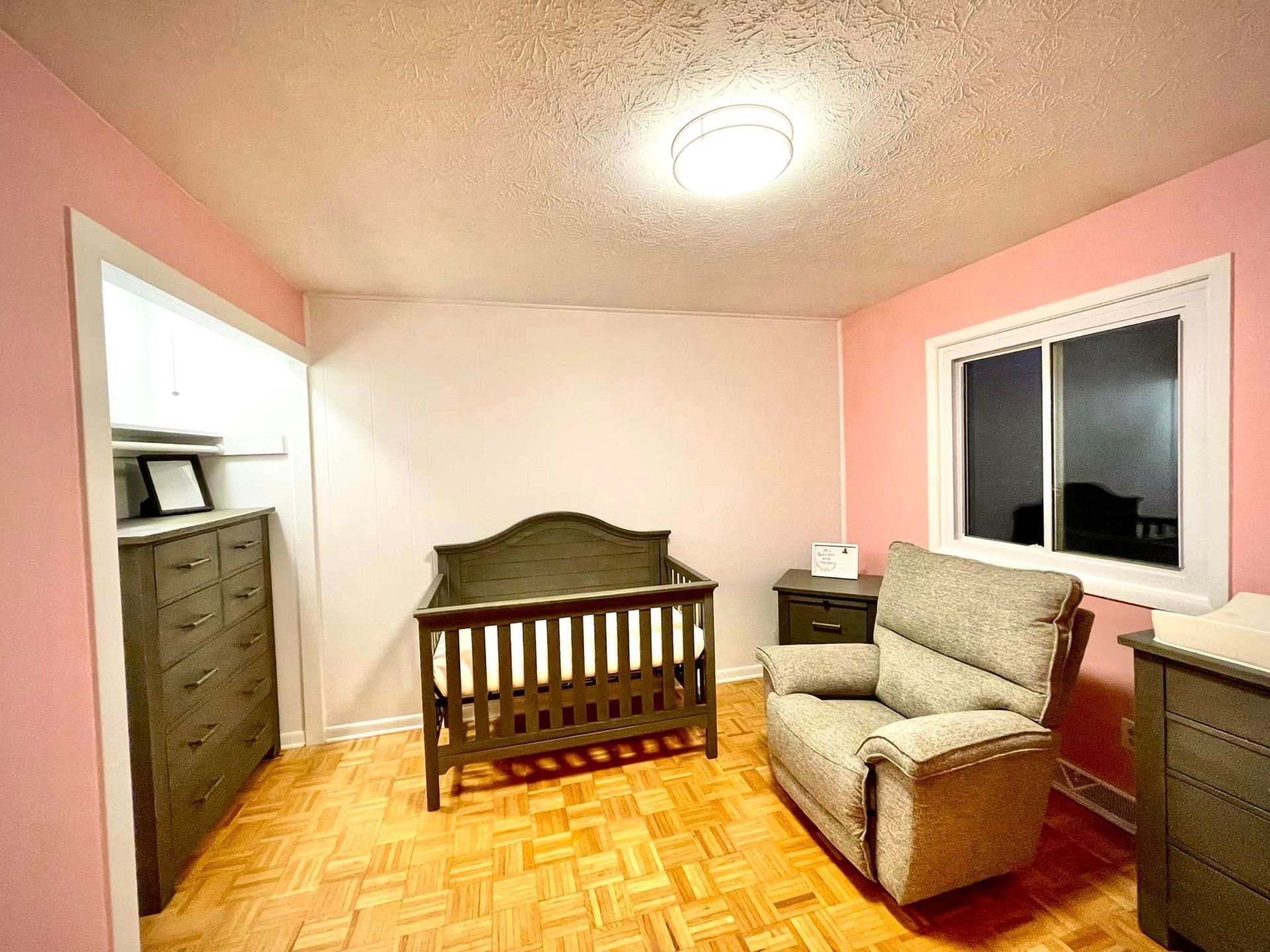 A baby room with a crib , chair , dresser , nightstand and window.