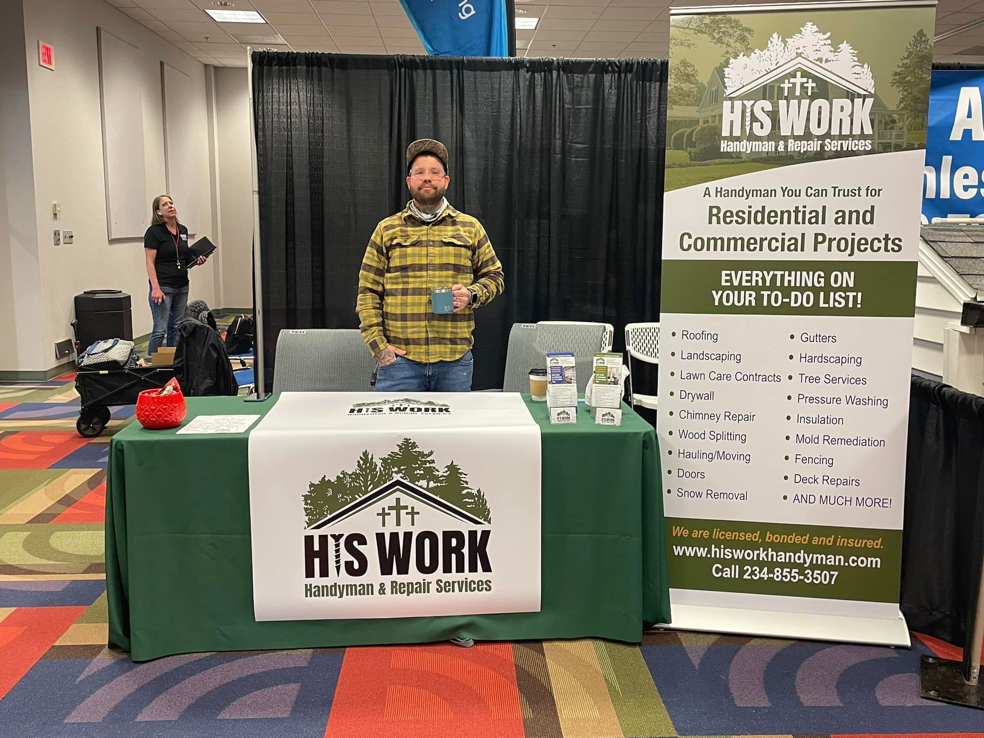 A man is standing in front of a table with a sign that says his work.