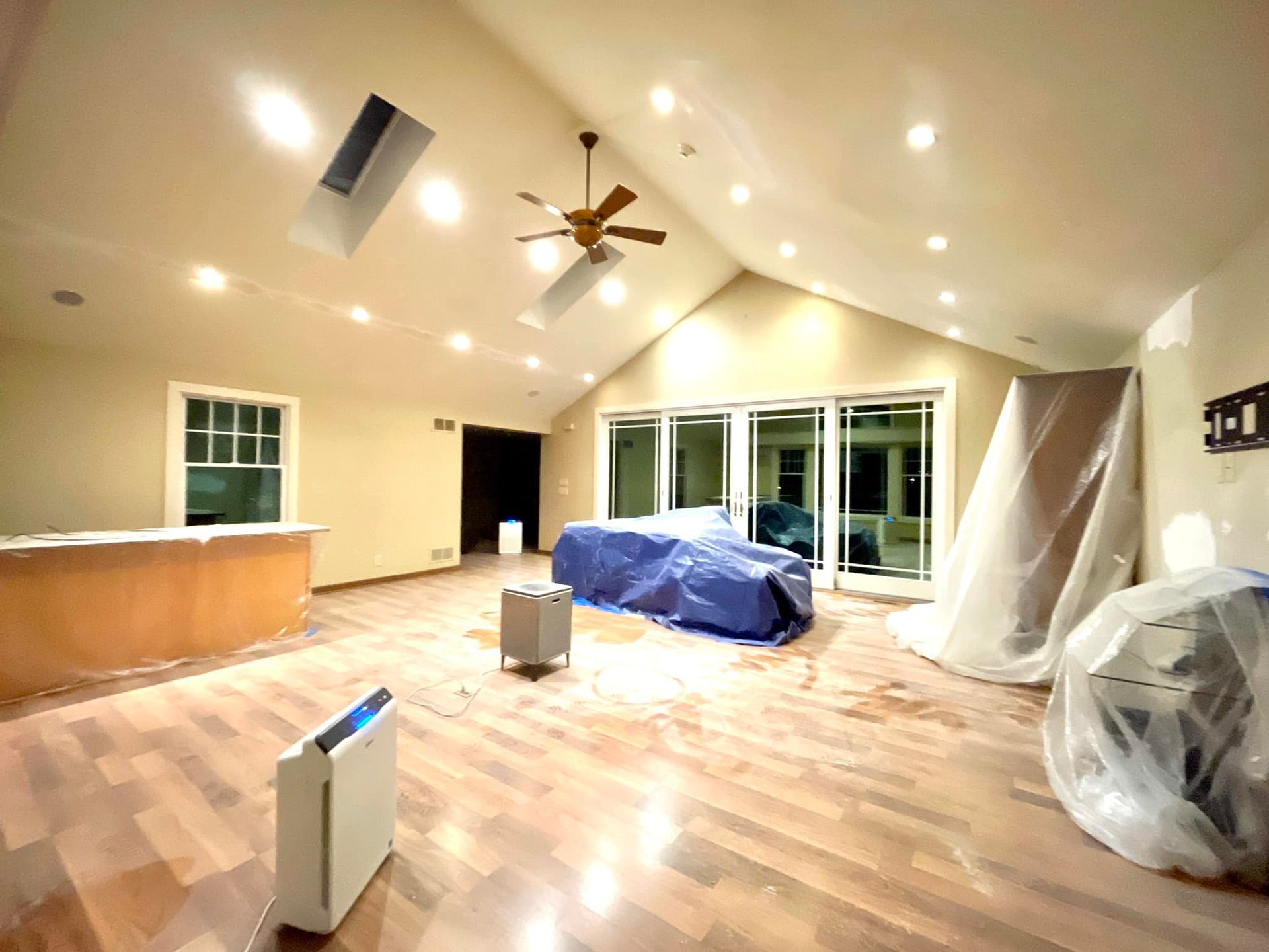 A living room with a ceiling fan and a blue tarp on the floor.