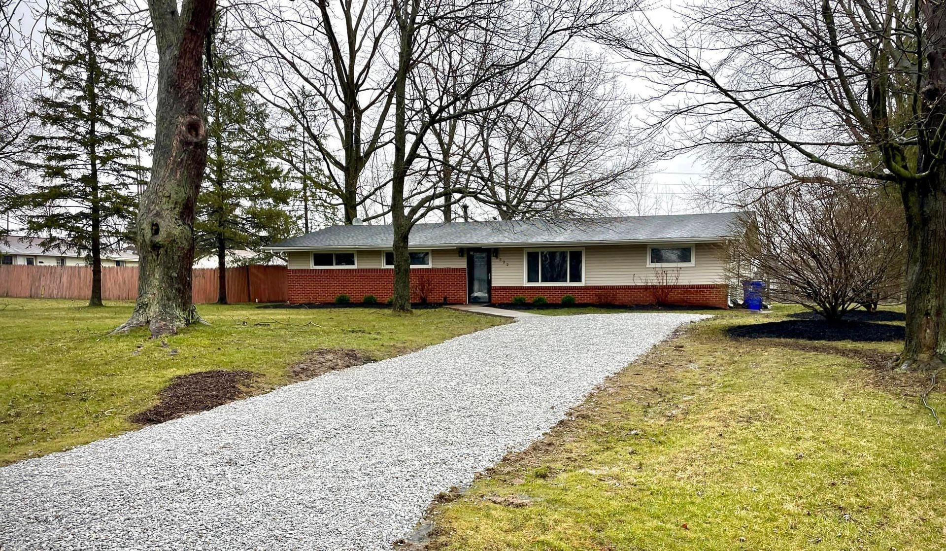 A house with a gravel driveway leading to it surrounded by trees.