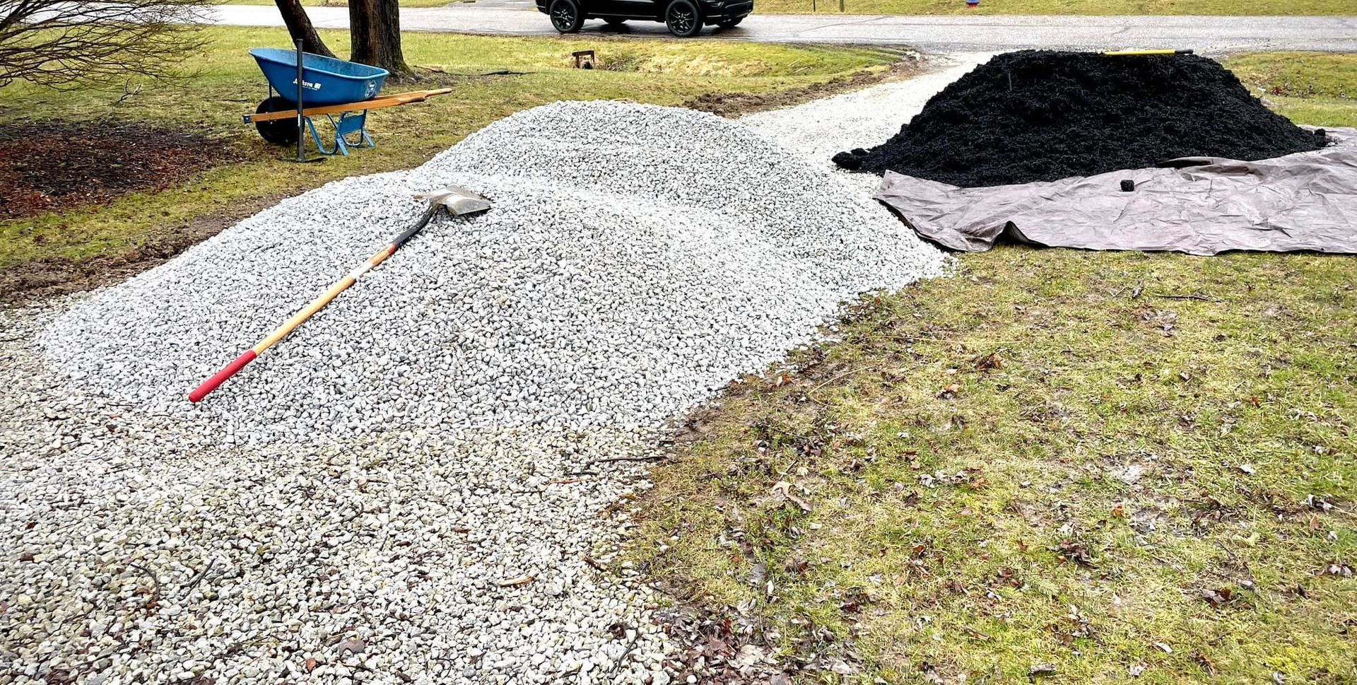 A pile of gravel with a rake and shovel on top of it.