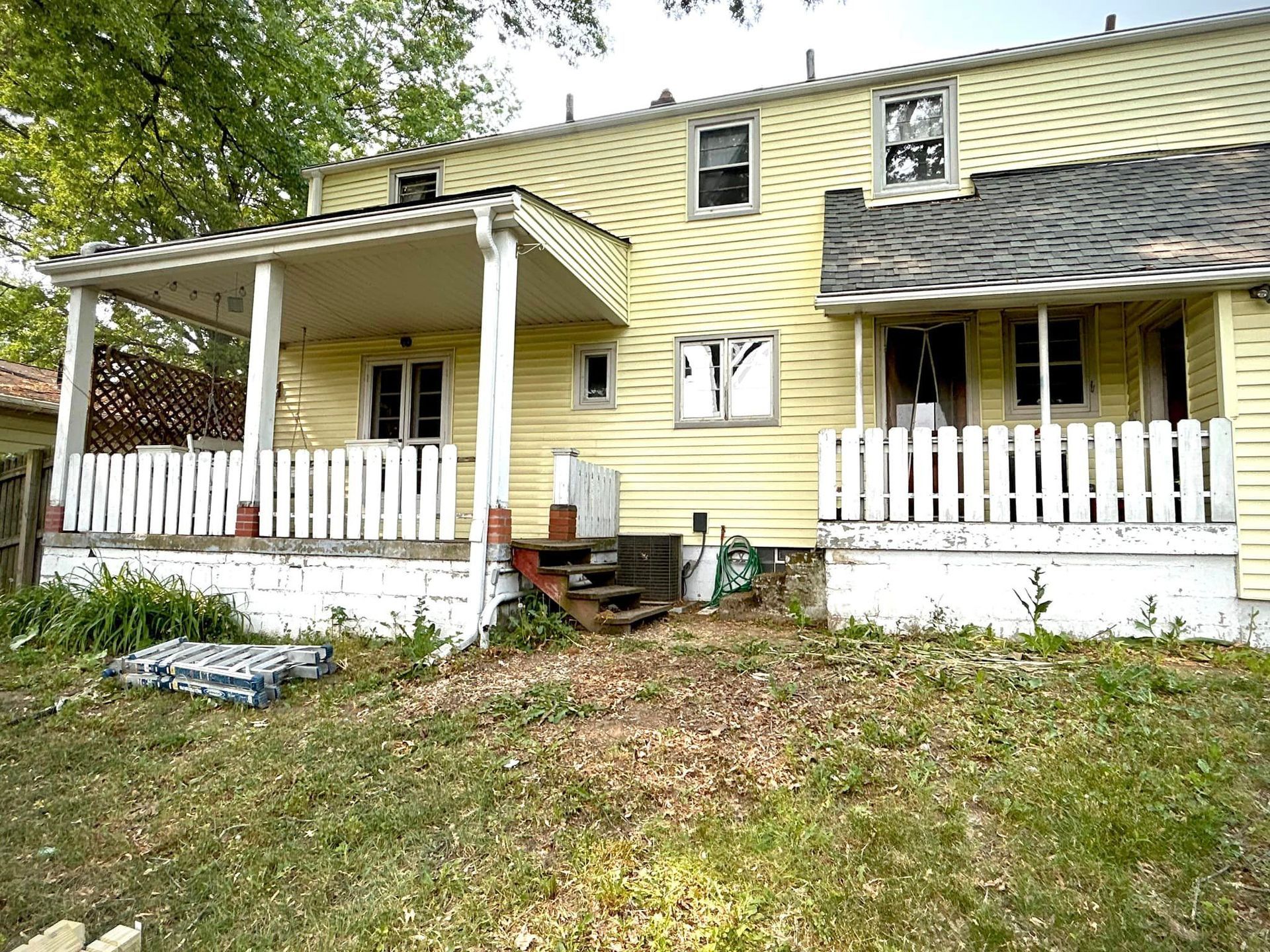A yellow house with a porch and a white picket fence.