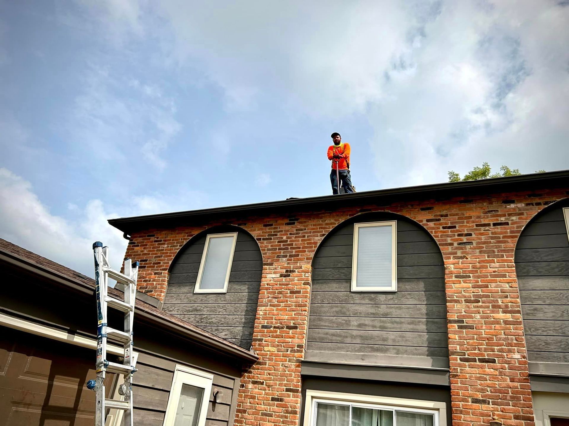 A man is standing on top of a brick building next to a ladder.