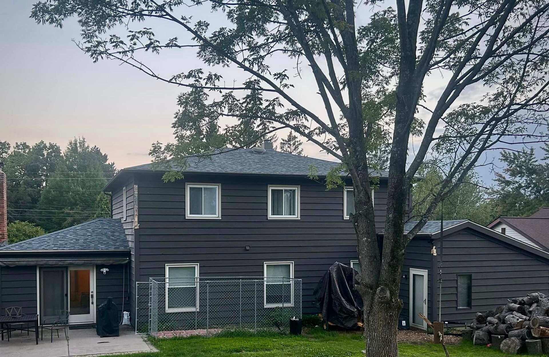 A black house with a blue roof and a tree in front of it