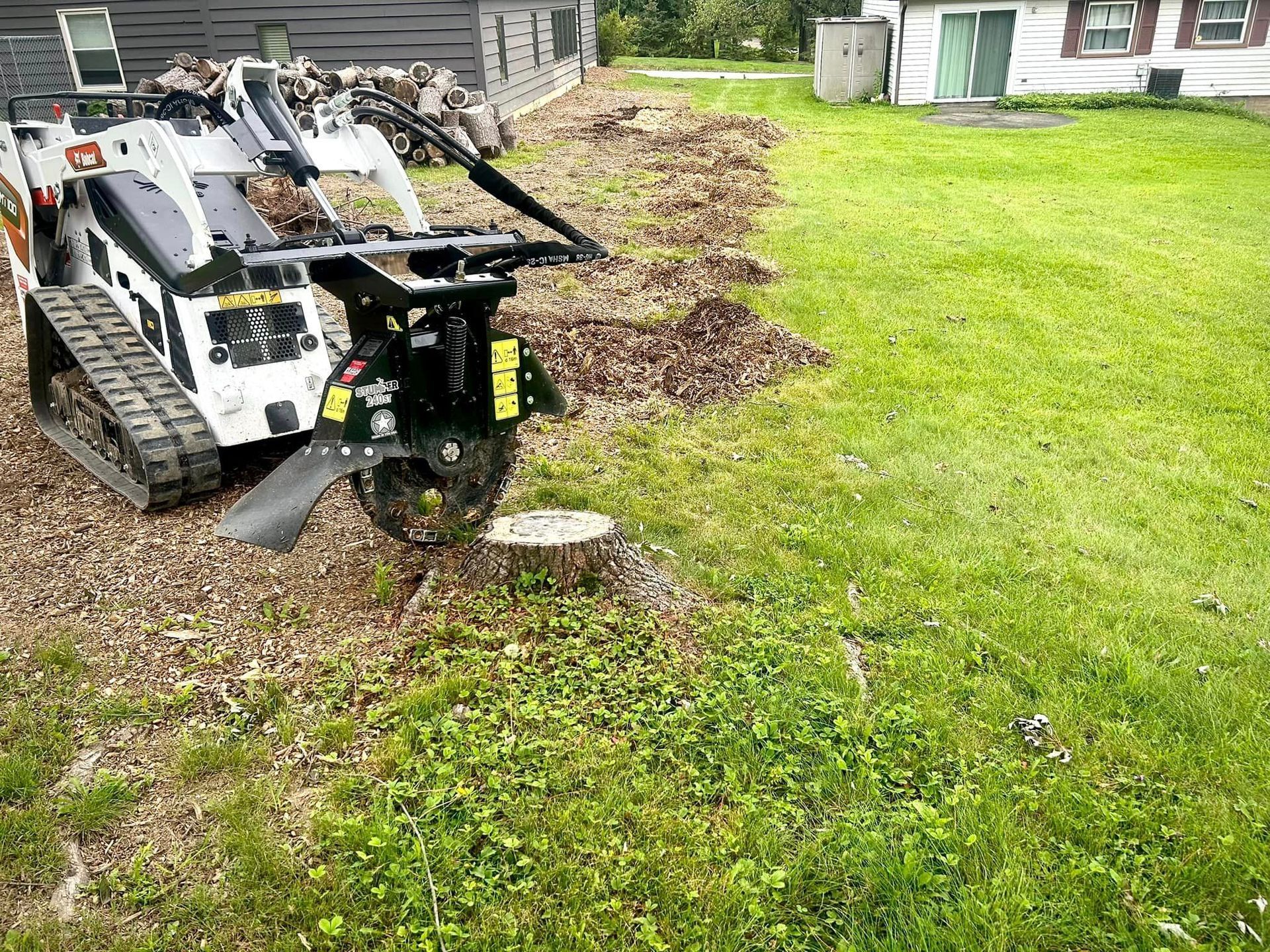 A stump grinder is sitting in the grass in front of a house.
