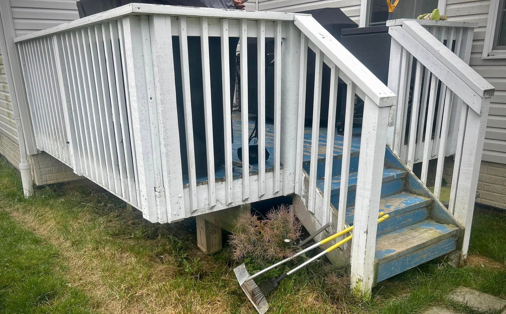 A white deck with blue stairs and a rake on it.