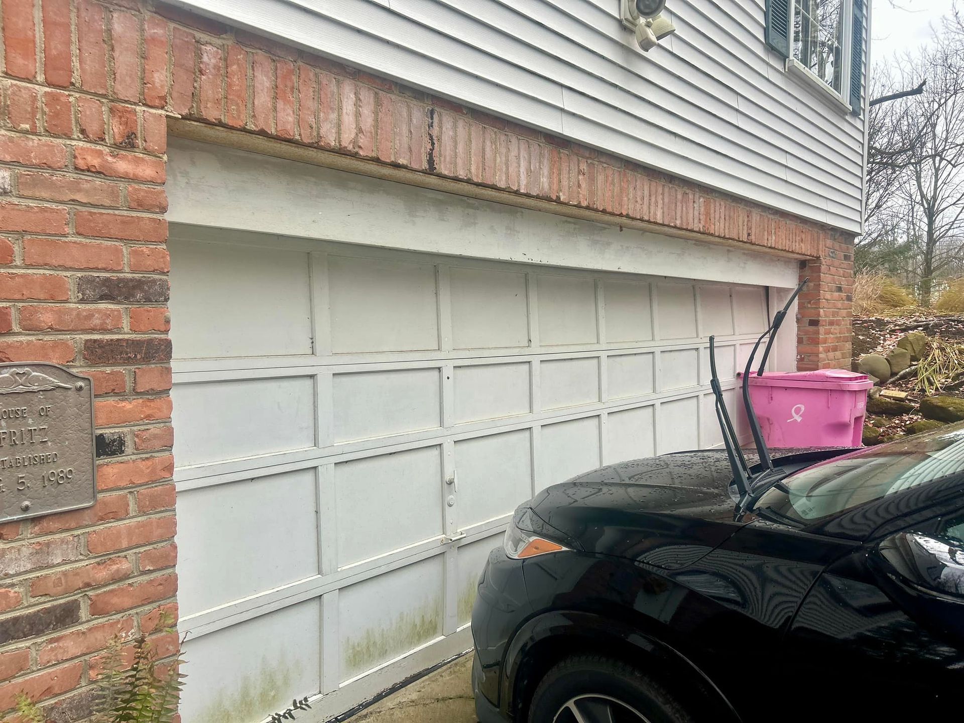 A black car is parked in front of a white garage door.