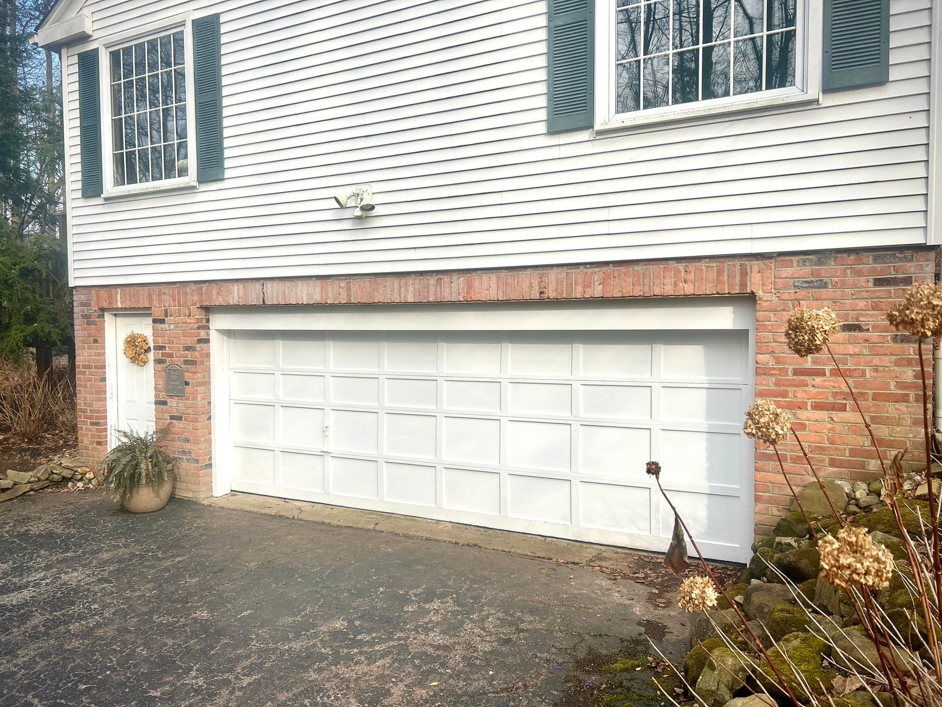A white garage door is on the side of a brick house.