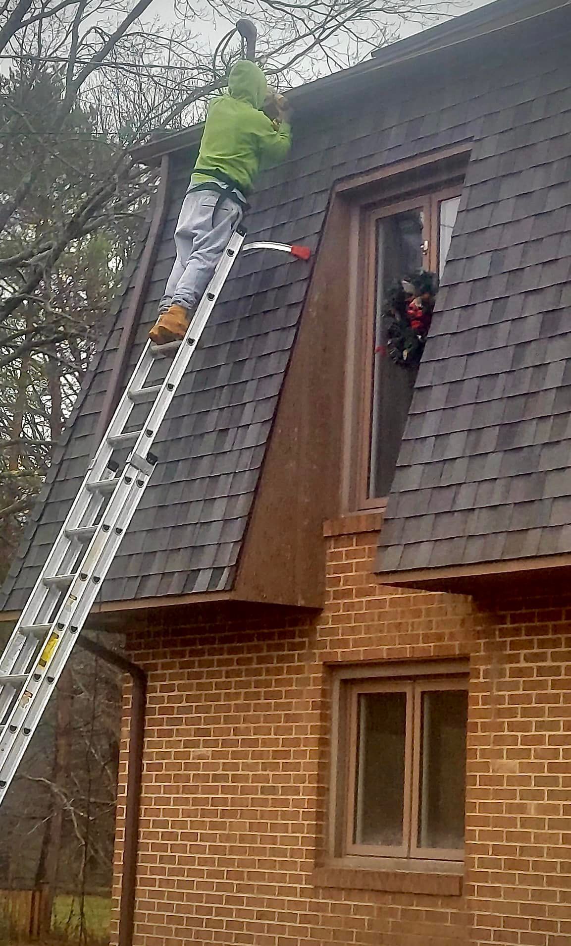 A man is standing on a ladder on the roof of a brick house.