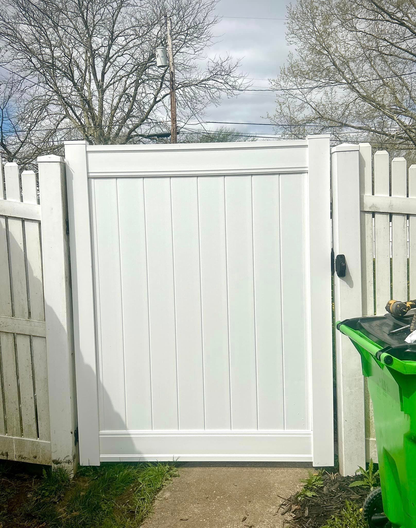 A white fence with a green trash can in front of it.