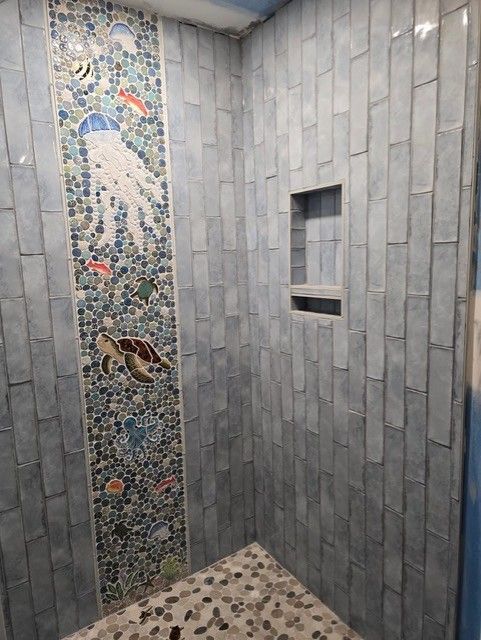 Blue tiled shower with a mosaic sea creature accent strip, featuring a jellyfish and sea turtle.