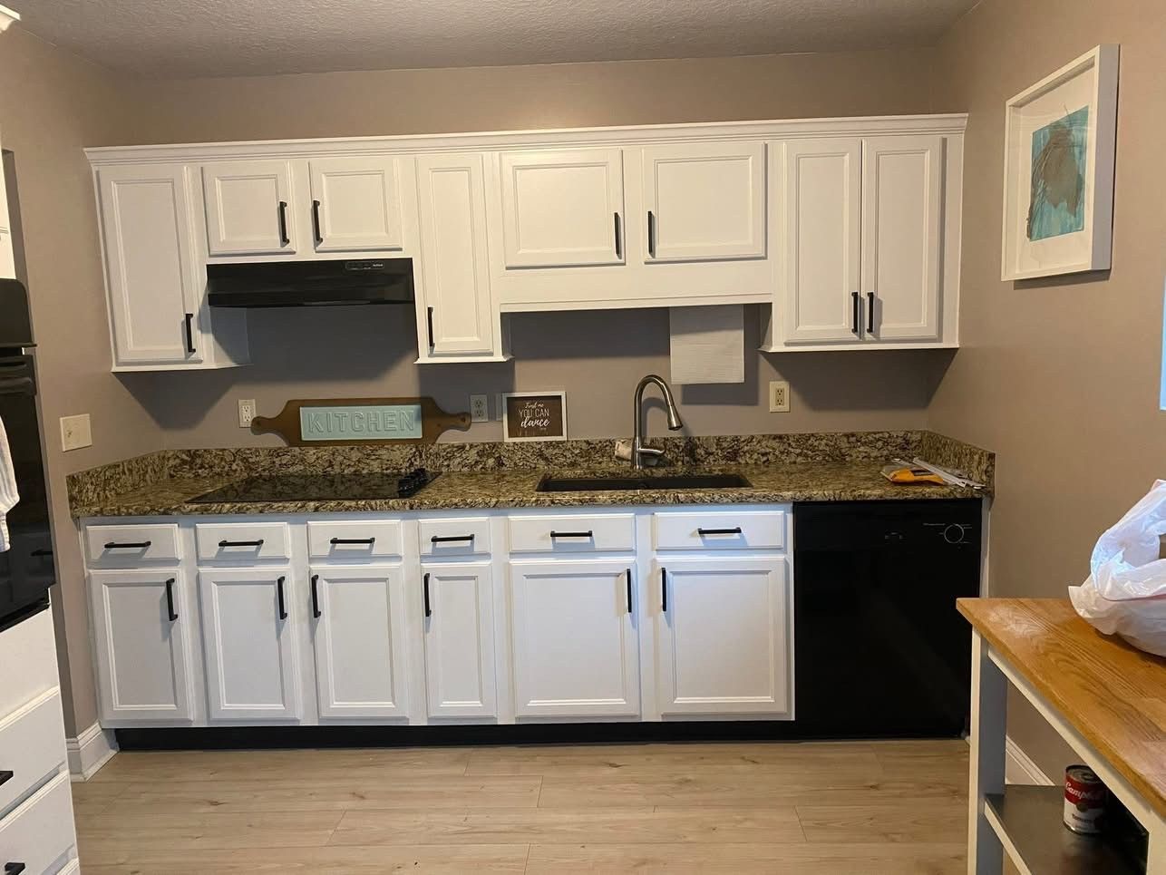 White kitchen cabinets with black hardware. Granite countertops, black appliances.