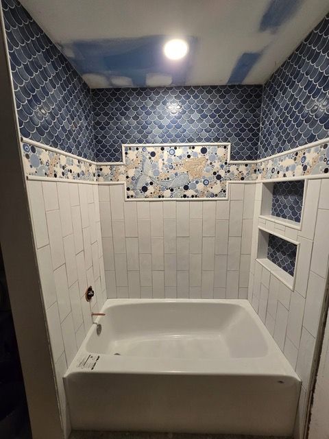 Bathroom with blue and white tile, tub, and built-in shelf. Ceiling has blue patterned tile.