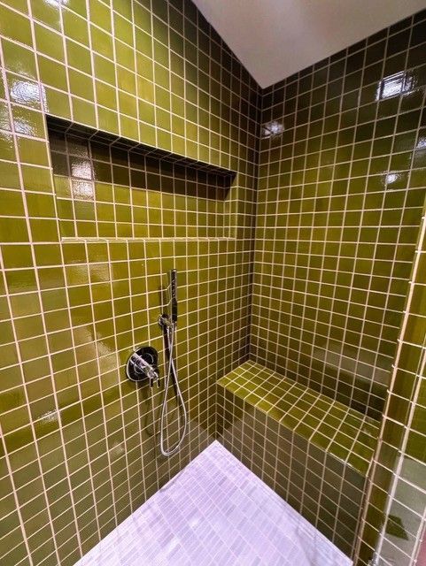 Green tiled shower with built-in bench and shelf. Silver shower head, white grout.