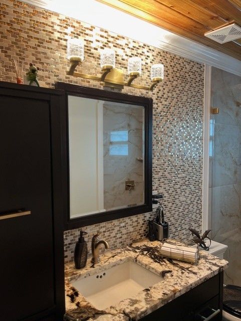 Bathroom with mosaic tile backsplash, vanity, mirror, and a light fixture.