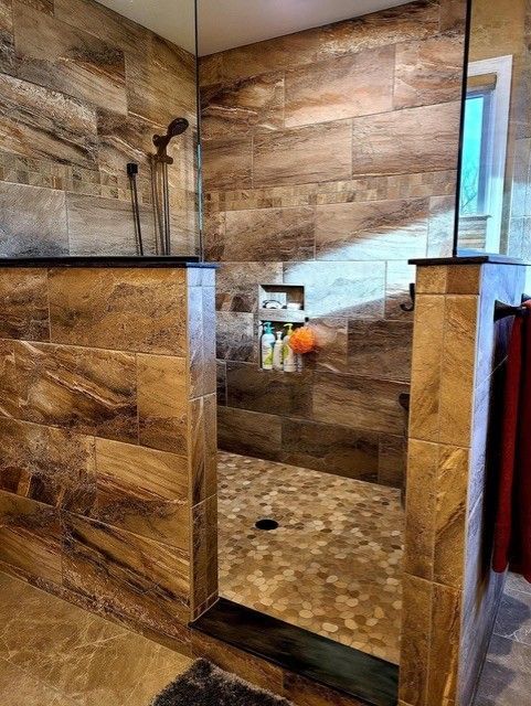 Shower with brown tiled walls and floor, glass enclosure, and built-in shelf.