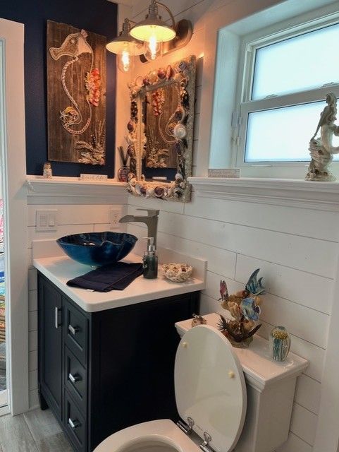 Bathroom with blue sink bowl, dark vanity, white shiplap walls, and nautical decor.