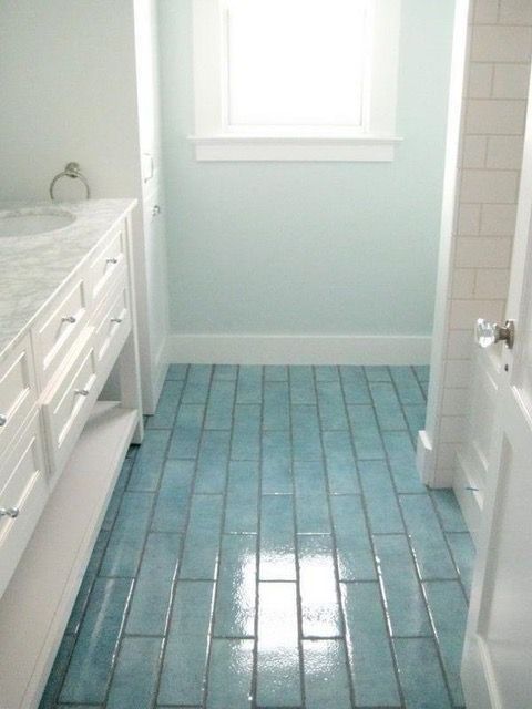 Blue-tiled bathroom floor, white vanity and door, light blue walls, window at end.