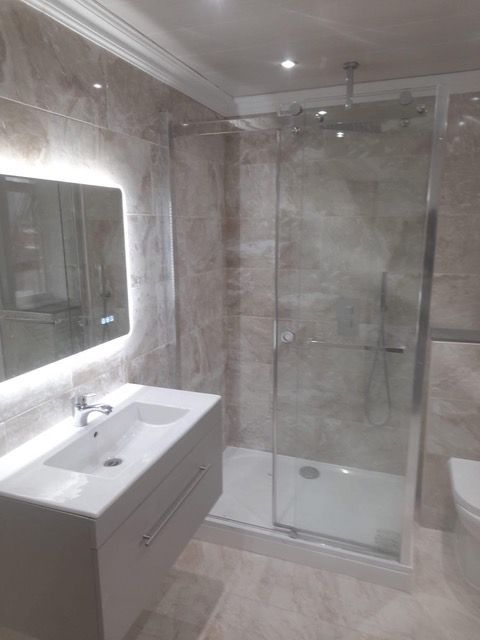 Modern bathroom with a glass shower, vanity with mirror, and light-colored tiles.