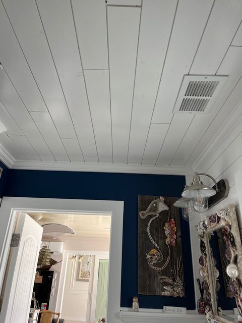 White plank ceiling in a room with blue walls, artwork, and a doorway.