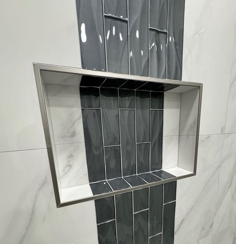 Built-in shower shelf with silver frame, white interior, and dark gray tile accent on a marble-patterned wall.