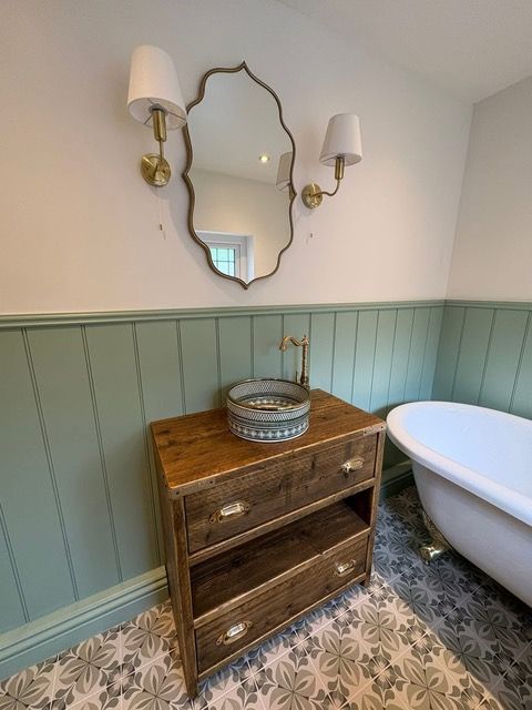 Bathroom with wooden vanity, patterned floor, clawfoot tub, and decorative mirror.