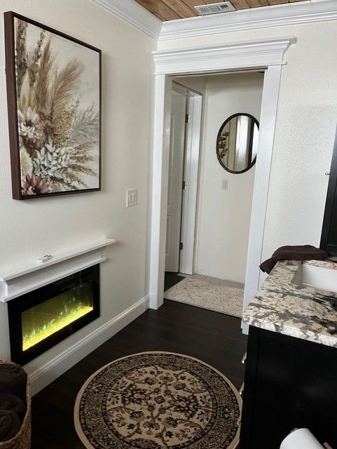 A room with a framed artwork, electric fireplace, and doorway leading to a bathroom with a circular mirror.