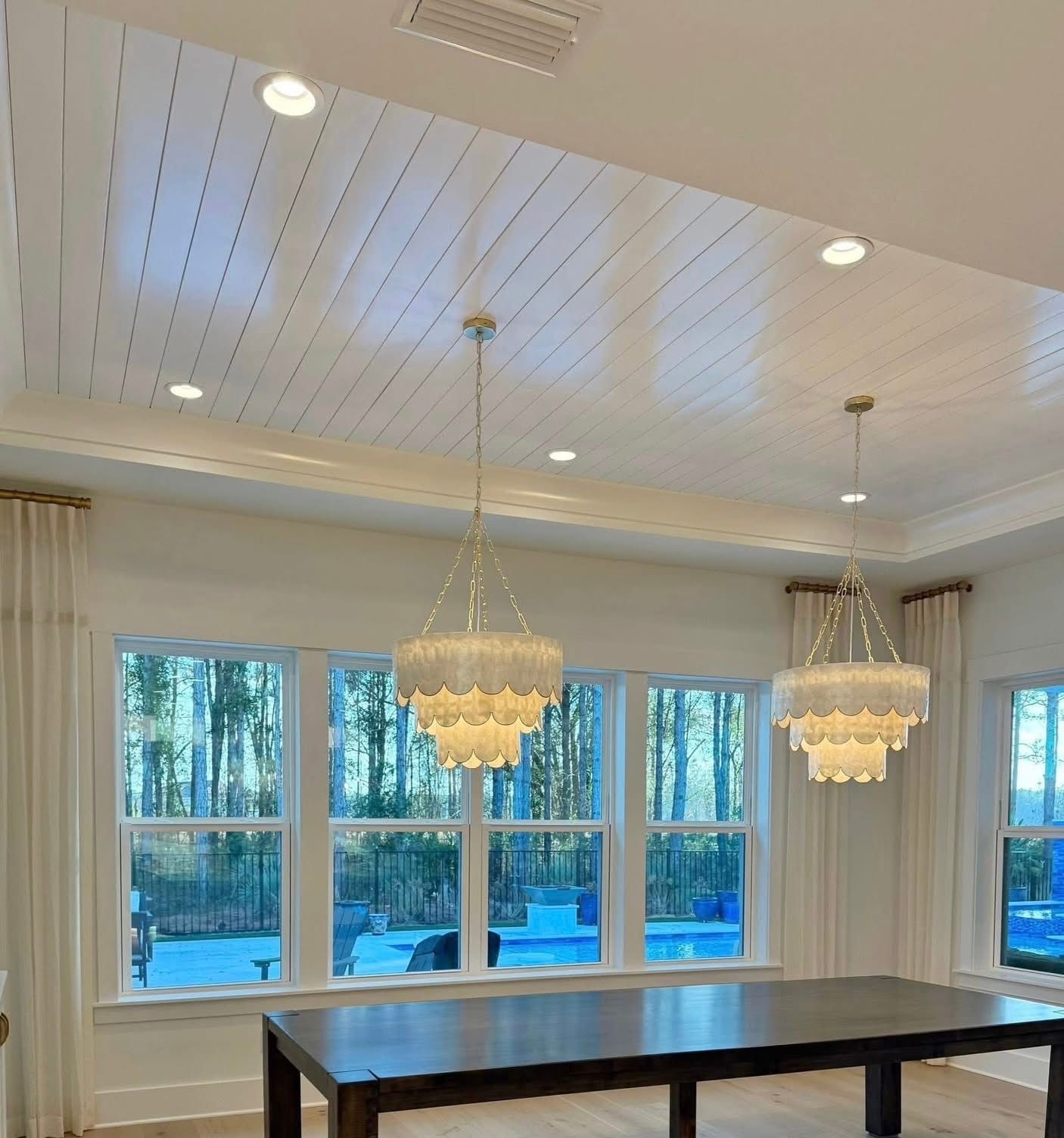 Dining room with chandeliers, windows, and dark wooden table.
