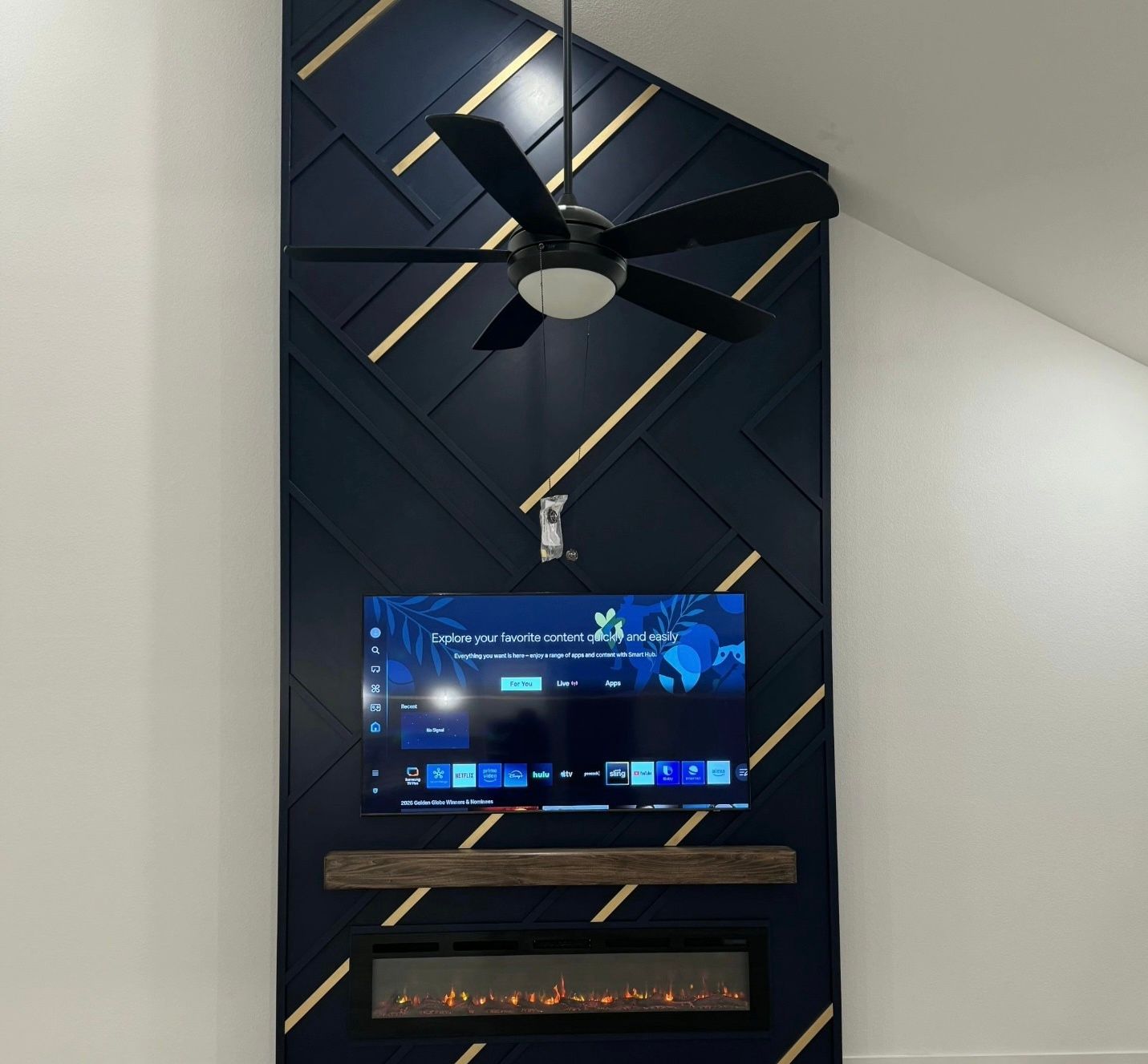 Navy blue accent wall with gold accents, TV, fireplace, and ceiling fan.