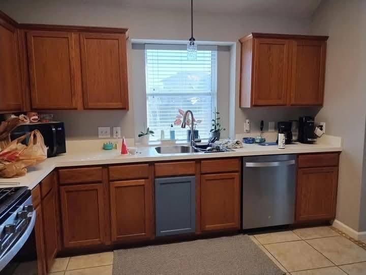Kitchen with brown cabinets, white countertops, and stainless steel appliances. A window is above the sink.