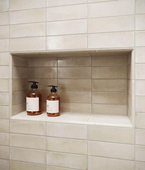 Recessed shower shelf with two brown pump bottles, beige tiled walls.
