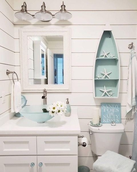 Coastal-themed bathroom with white shiplap walls, a light blue glass sink, and a boat-shaped shelf with starfish.