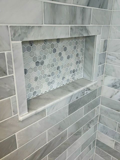 A recessed shower niche with marble tiles and a hexagon tile back, in a gray bathroom setting.