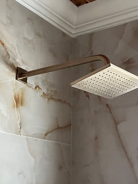 Square showerhead on a metal arm against marble tile.