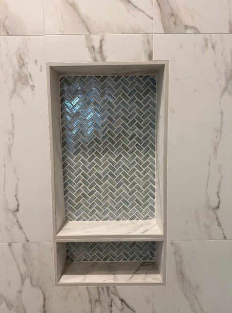 Recessed shower niche with herringbone tile pattern, marble-like surround, installed in a tiled wall.