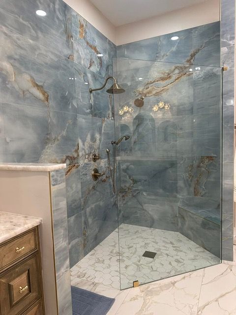 Blue-tiled shower with glass door and marble floor, bronze fixtures.