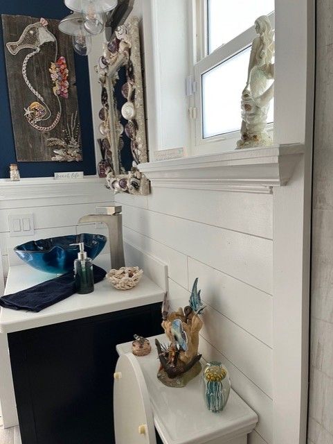 Coastal-themed bathroom with a blue glass sink, white wainscoting, and seashell artwork.