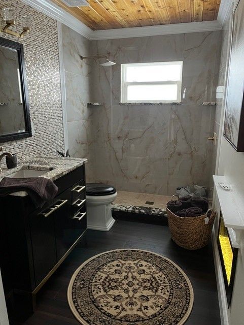 Bathroom with black vanity, mosaic wall, and walk-in shower. Dark wood floor, patterned rug, and wooden ceiling.