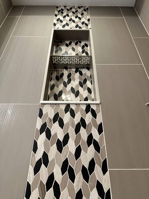 Bathroom shower niche with gray, black, and beige patterned tile.