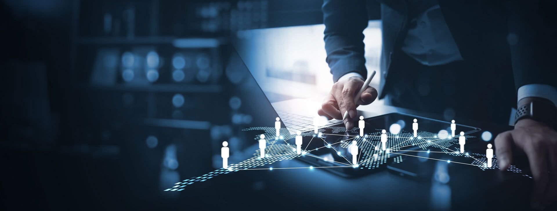 Business meeting around a table. Two men shaking hands, others watching, with laptops and documents.