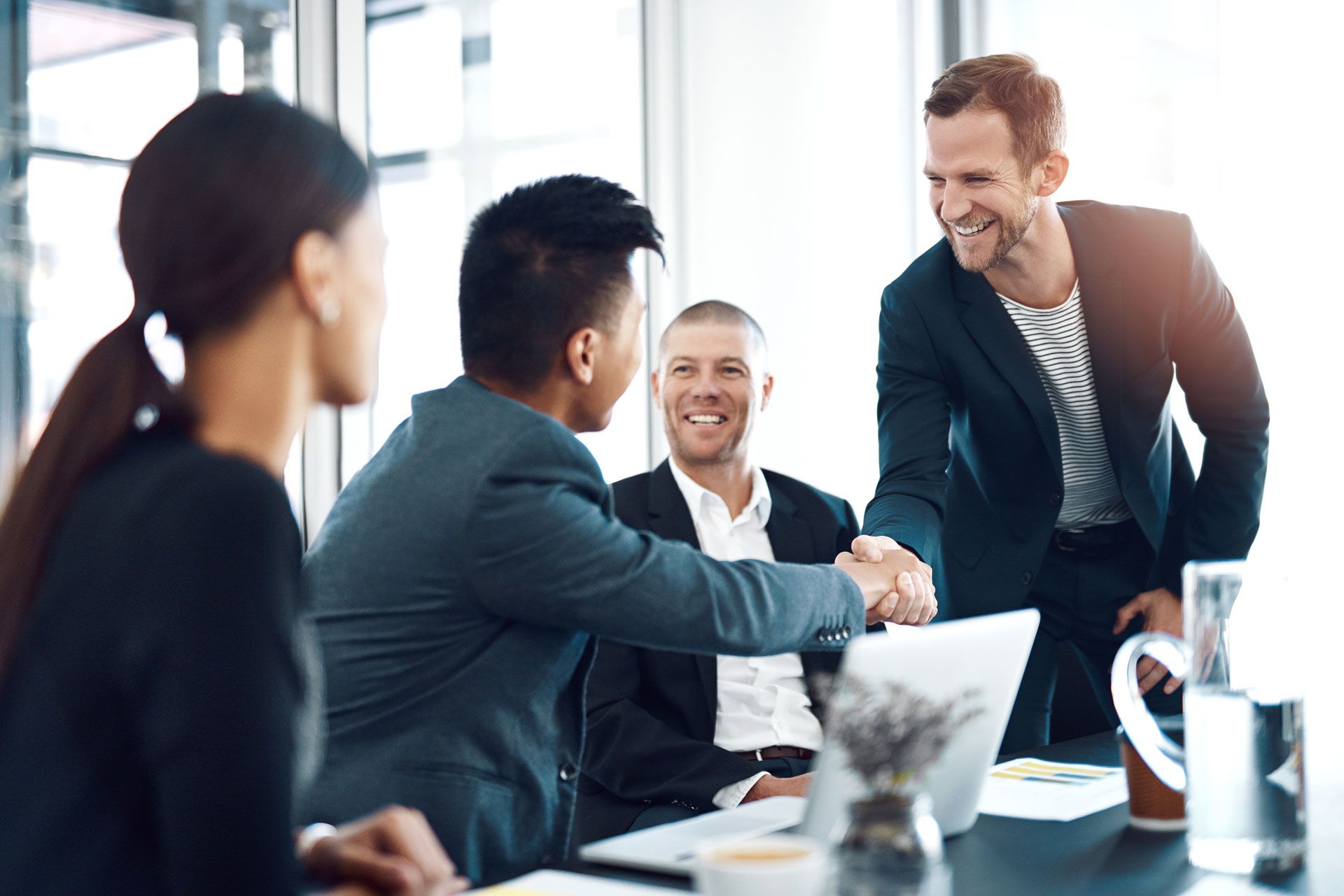 Business colleagues shaking hands in a bright office, smiling.