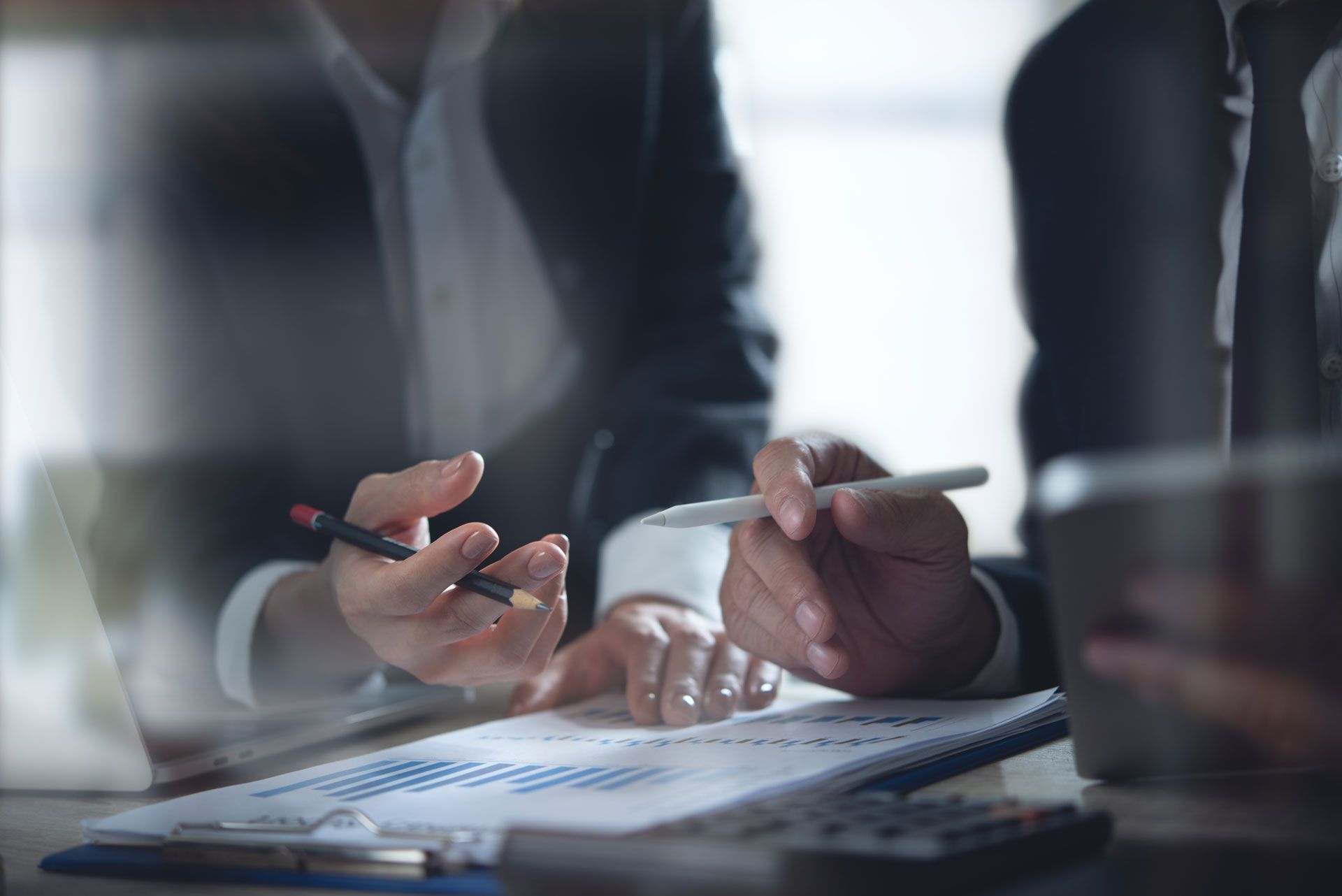 Two people in business attire reviewing financial documents, discussing data analysis.