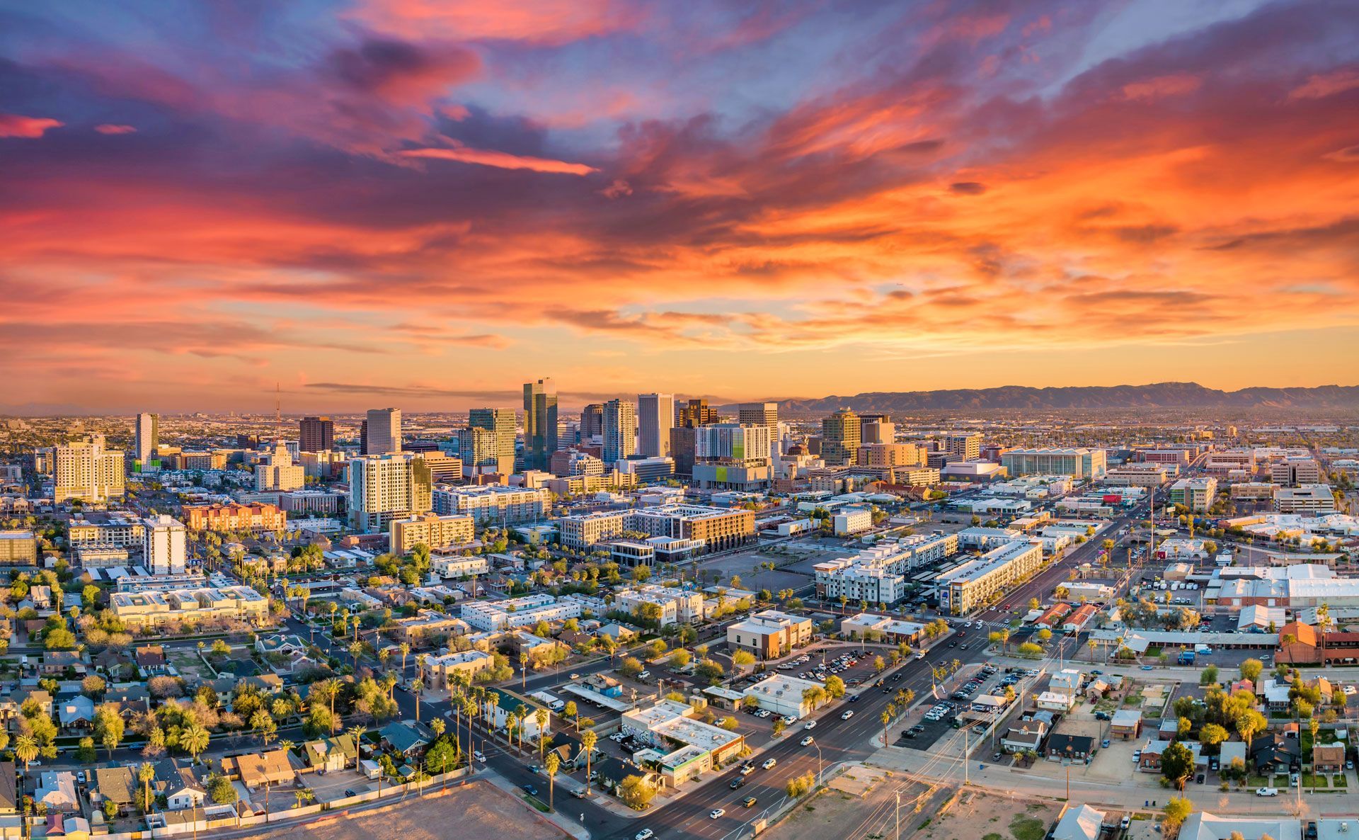 City skyline under a vibrant sunset with orange and purple clouds.