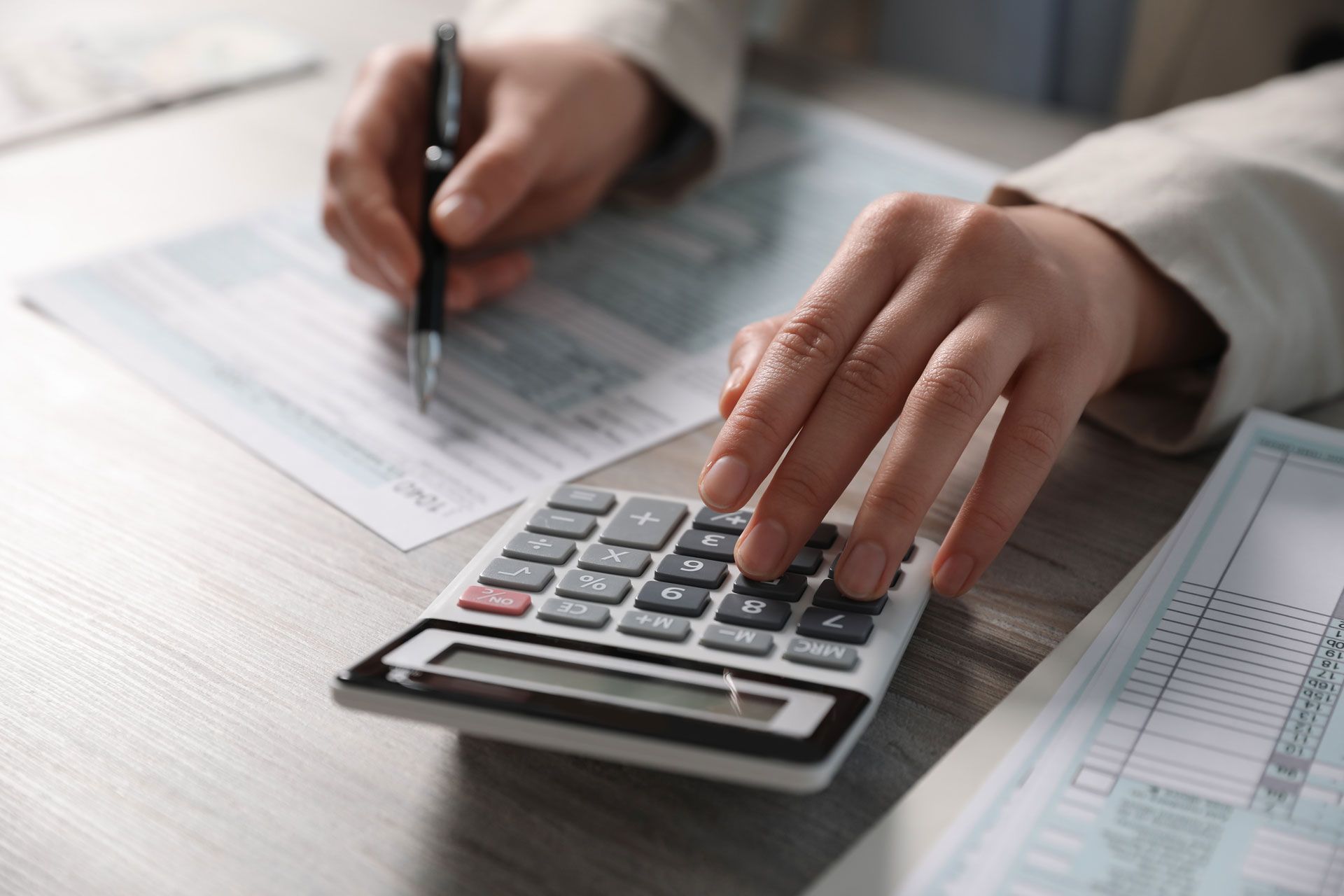 Hands using calculator and pen, completing paperwork on a desk.